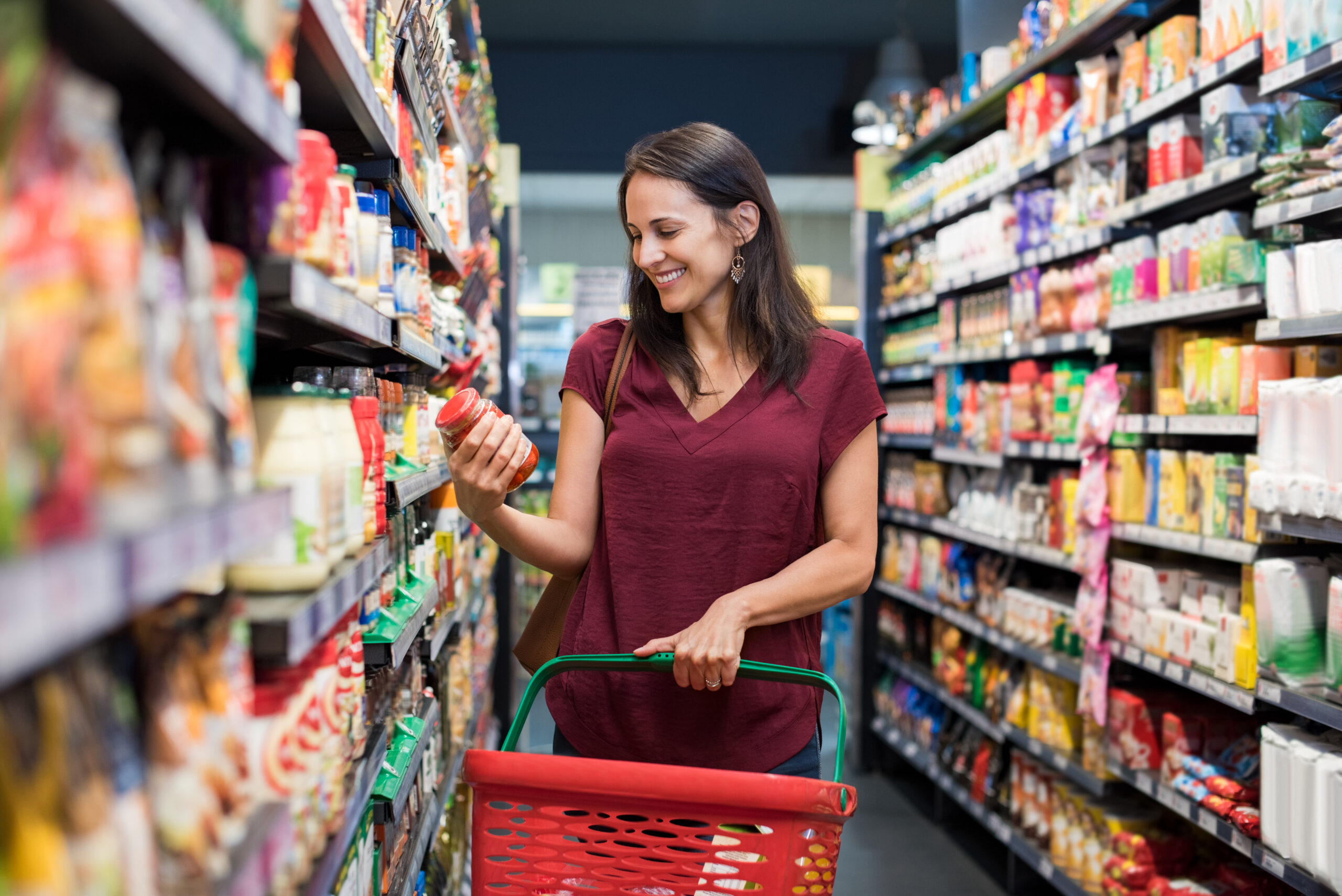 Happy mature woman looking at product at grocery store. Smiling hispanic woman shopping in supermarket and reading product information. Costumer buying food at the market.